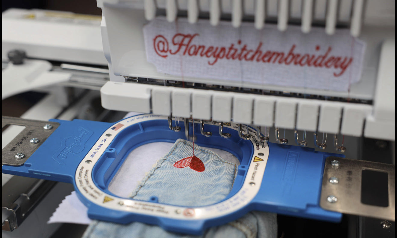 Embroidery machine with a heart design on fabric and 'Honeypitchembroidery' branding.